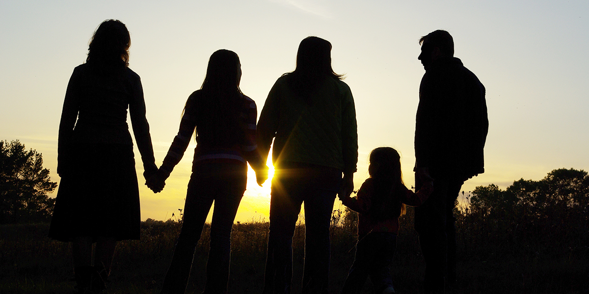 En familj på fem håller händer i en solnedgång i motljus