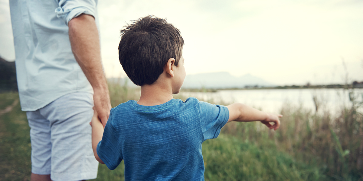 En liten pojke håller hånden till en vuxen medan han pekar ut mot en sjö