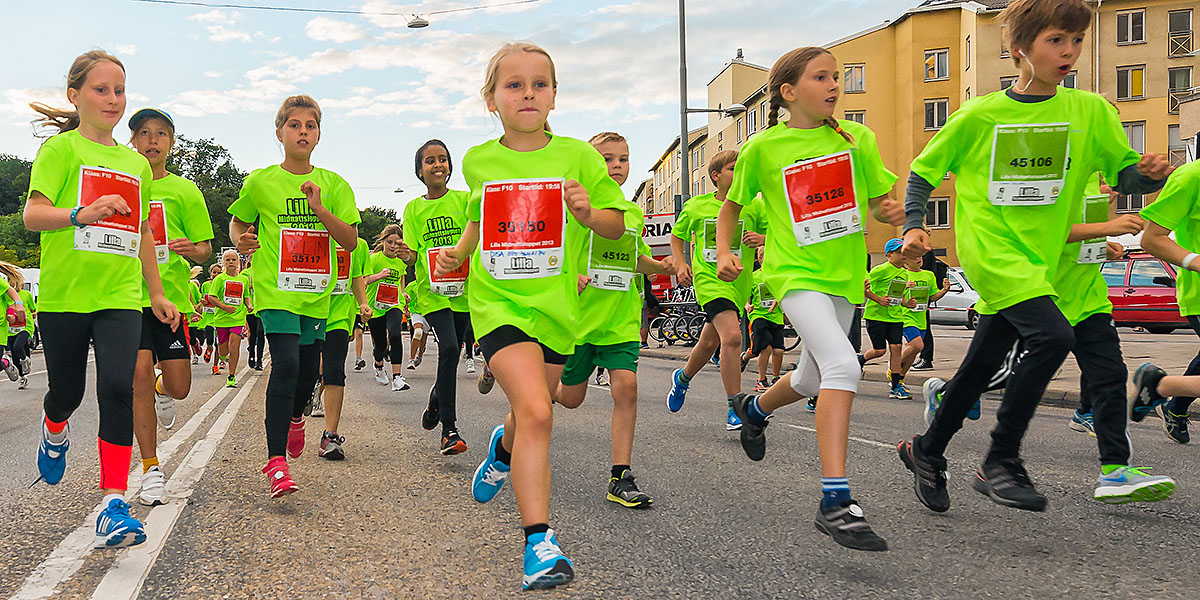 Löpande barn i gröna t-shirts som kör ett lopp